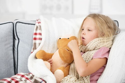 En syk jente som sitter med en bamse og hoster.