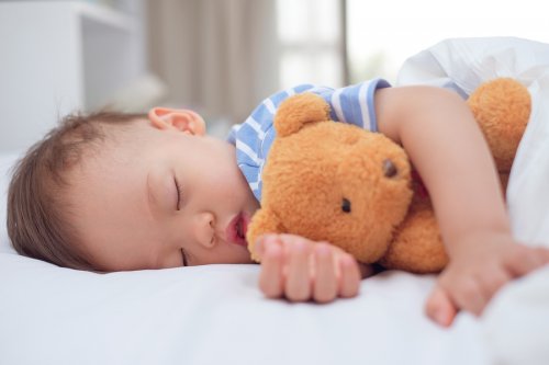 Et barn som sover med en bamse i armene.