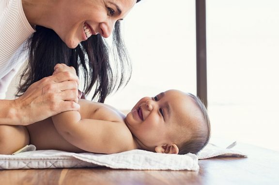 En mor lent over en baby på et bord.