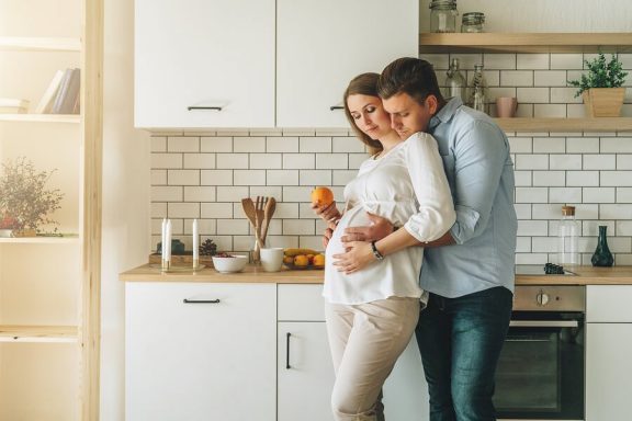 Et gravid og lykkelig par på et kjøkken.