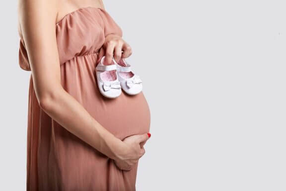 En gravid kvinne som holder et par små babysko.