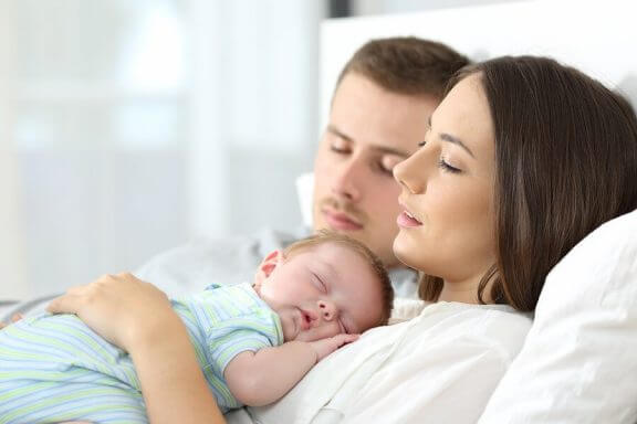 Et par som ligger med en baby på brystet.