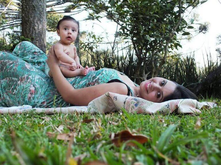 En mor ligger på et teppe med en baby på magen.