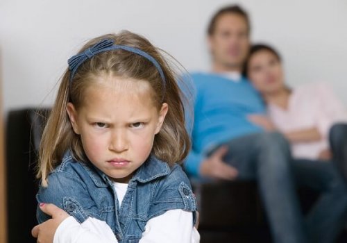 En sint jente sitter foran foreldrene sine