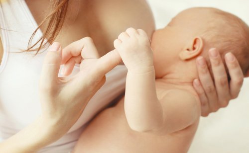 En baby holder fingeren til moren sin mens han eller hun ammer.