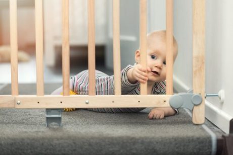 En baby bak en trappegrind, som gjør hjemmet babysikkert.