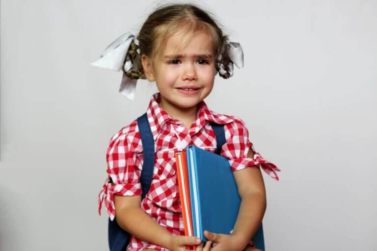 Liten jente med flette i håret og bøker i armene gråter.