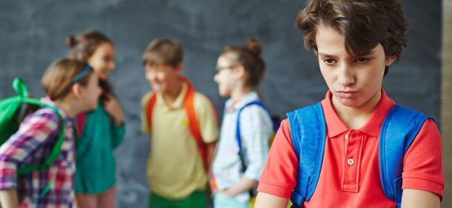 Flere barn står sammen og ler, gutt står alene og er lei seg.