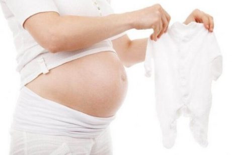 En gravid kvinne ser på babyklær.