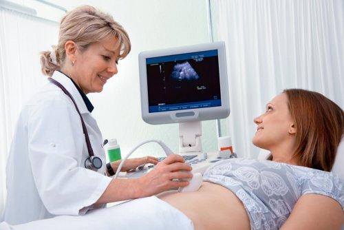 En gravid kvinne smiler under en ultralyd.