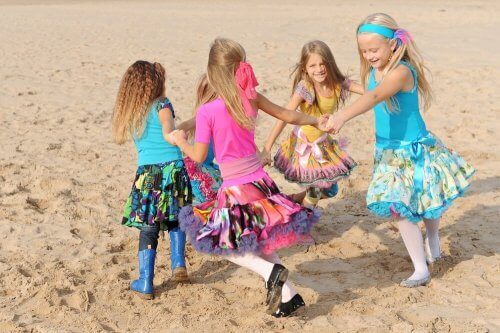 Små jenter i kjoler som løper i ring på stranden.