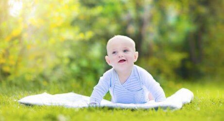 En baby som sitter alene på et teppe ute på gresset
