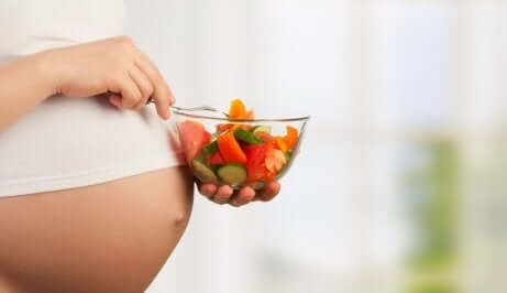 En gravid kvinne som spiser frukt fra en skål.