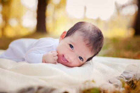 En liten baby som ligger på et teppe ute