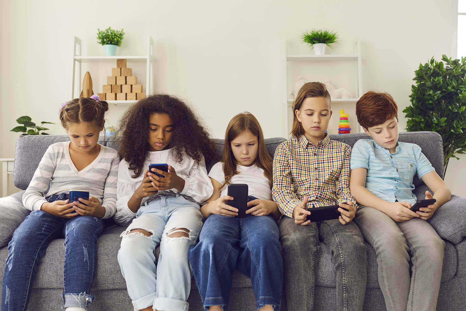 Fem barn som sitter i sofaen og ser på telefonene sine