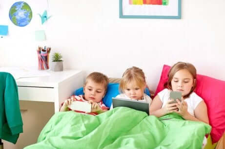 Tre barn som ligger i en seng og spiller spill